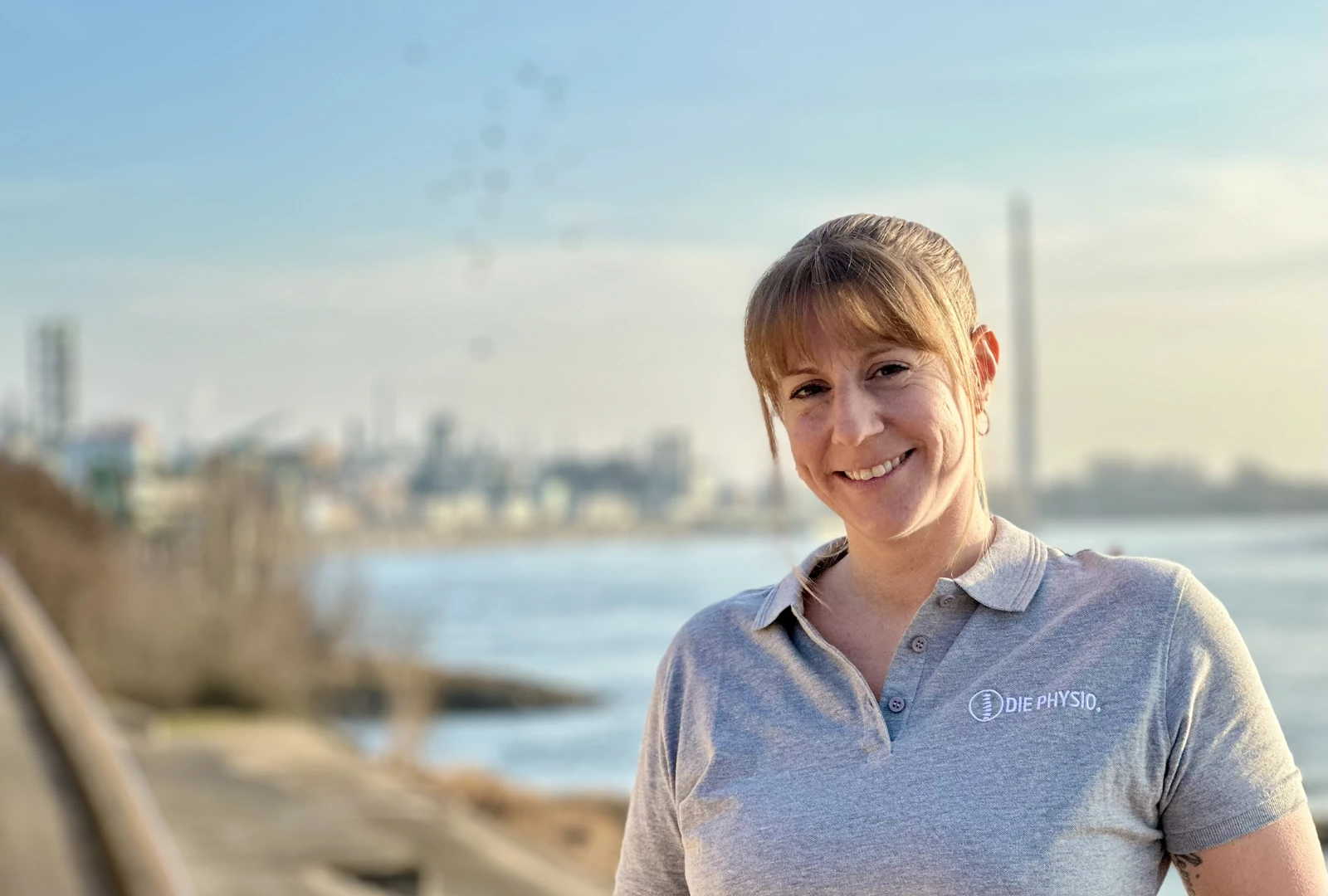 Mobile Physiotherapeutin Daniela Lindemeier in Leverkusen vor der Kulisse des Bayerwerks am Rhein